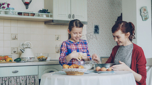 可爱的小女孩帮助她的母亲在厨房里将饼干面团搅拌到碗里。