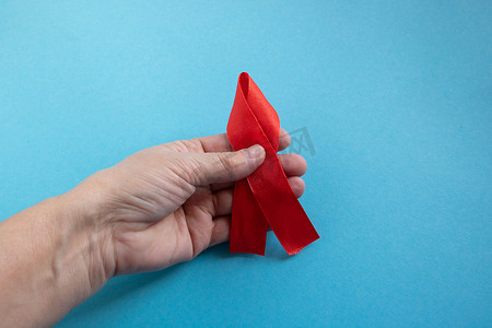 一只手握着蓝色背景上的红丝带 — 世界艾滋病日、捐助者日、血友病日的概念