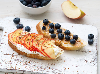 乳清摄影照片_健康早餐，包括甜三明治 — 意大利乳清干酪、蓝莓、苹果片、花生酱