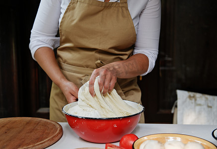 碗红色摄影照片_细节：在乡村厨房里准备面包时，厨师的手在老式搪瓷红色碗中揉捏发酵面团