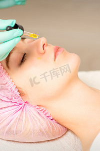 年轻的白人妇女在美容诊所用移液器去除酸性有机视黄醇去皮面部皮肤。