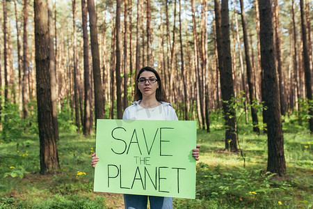 年轻女活动家站在树林里，举着拯救地球的海报，一名志愿者与森林砍伐作斗争