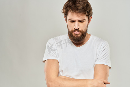 一个身穿白色 T 恤、留着胡须的男人对面部表情浅色背景感到不满