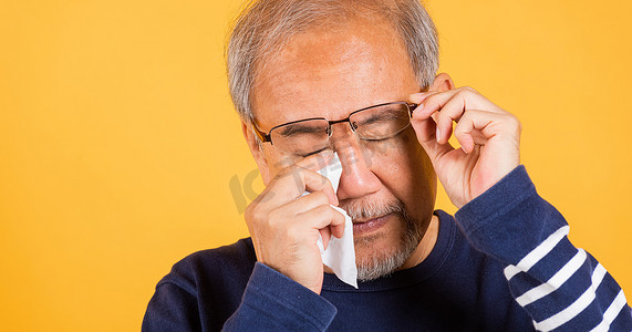 擦摄影照片_亚洲老人哭着举起眼镜用纸巾擦红眼睛