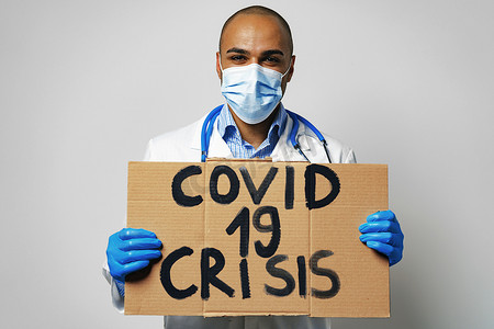 抗议者摄影照片_抗议者手中的“Covid-19 危机”标语牌。