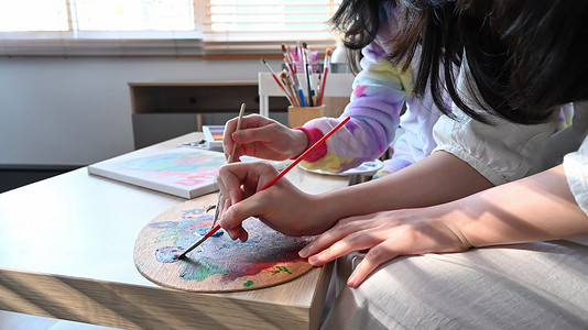 裁剪拍摄两个女孩在艺术课上用水彩画画。