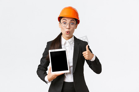 令人印象深刻和兴奋的亚洲女工程师、穿着西装和安全头盔的工业技术人员竖起大拇指，数字平板电脑屏幕上带着惊奇的表情，对利润图做出反应