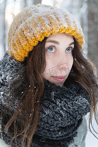 在白雪皑皑的森林的背景下，一位戴着鲜艳的羊毛帽子和围巾的微笑的年轻白人女子的画像。