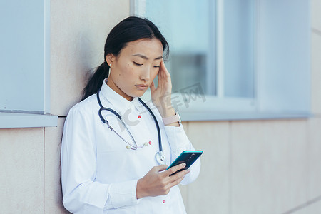 悲伤的亚洲医生护士，在休息时在诊所附近使用电话，女人严重头痛