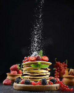 新鲜水果摄影照片_黑色背景上一堆煎饼，上面放着新鲜水果，上面撒着糖粉