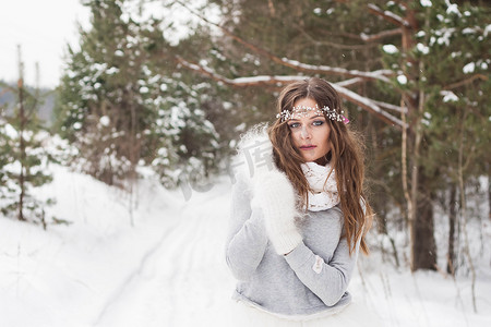 美丽的新娘穿着白色连衣裙，在冰雪覆盖的冬季森林里捧着花束。