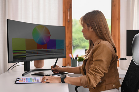 使用图形输入板和专业计算机在家庭办公室从事设计项目的年轻创意女性