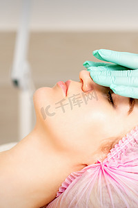 保湿面膜摄影照片_戴着手套的美容师在女性脸上涂上带去角质霜的保湿面膜。