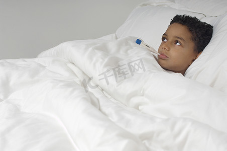 一个非洲裔美国男孩躺在床上，带着温度计