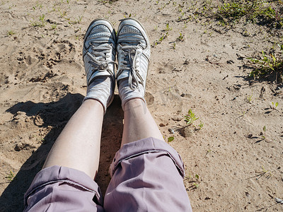 穿着粉色裤子和白色运动鞋躺在沙滩上的女人的腿