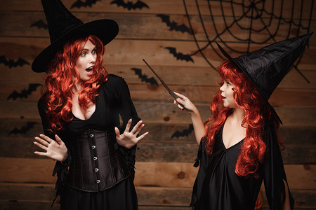 万圣节概念-小红发女巫用魔杖对她的母亲使用魔法，表情震惊。