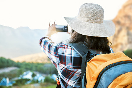 徒步旅行的女人在大自然中用手机拍摄冒险照片，在徒步旅行中留下回忆，并在度假时欣赏乡村的美丽景色。
