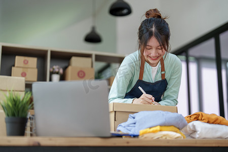 一家小型初创公司的肖像，中小企业老板，一位亚洲女企业家，正在记事本上写下信息以整理产品，然后将其包装到客户的内盒中