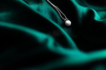 深翠绿色丝绸背景的豪华白金珍珠项链，节日魅力珠宝礼物