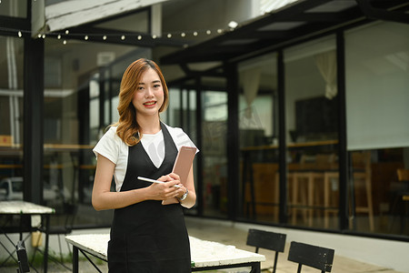 咖啡店老板穿着围裙站在咖啡店门外，对着镜头微笑的肖像