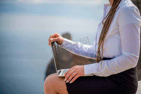 一个女人坐在露台上，在 macbook 键盘上打字，可以欣赏到美丽的海景。