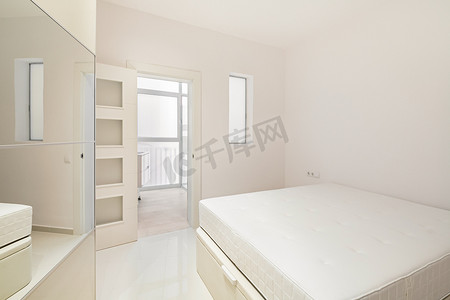 现代翻新公寓中的白色卧室配有床、衣柜和浴室入口，可供出租。