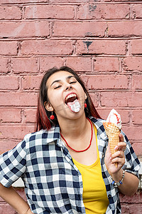 在街上粉色砖墙背景上吃冰淇淋的红头发开朗时髦女人