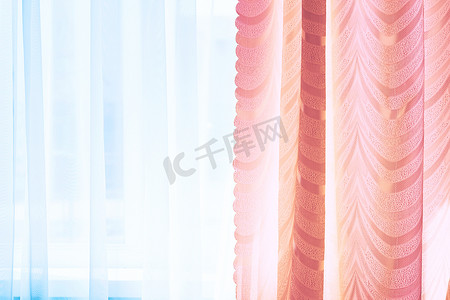 在温暖的正午阳光下，窗户上的粉色窗帘和蓝色薄纱