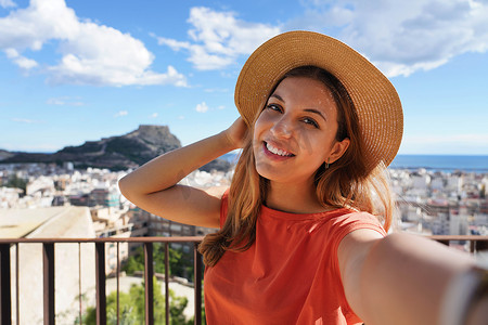圣费尔南多城堡的旅游女孩与阿利坎特城市景观和贝纳坎蒂尔山的自拍合影，背景是圣巴巴拉城堡。