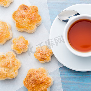 桌子俯视摄影照片_传统早餐，包括一杯茶和甜糕点 — 烤饼、一杯茶、勺子，在木制蓝色桌子上，俯视。