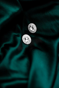 深翠绿色丝绸上的豪华钻石耳环，节日魅力珠宝礼物