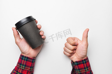 一个男人的手一手拿着白色背景上的空纸黑杯咖啡，另一只手则表现出阶级的手势，竖起大拇指
