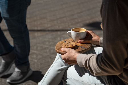 坐在街边咖啡馆的男人，木托盘上放着咖啡和饼干