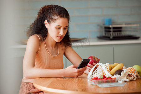 在电话上进行苹果研究的女性的饮食、健康心态和保健食品。在家阅读减肥、烹饪和营养的年轻女性营养师在厨房里拿着在线水果