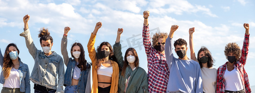 多种族活动抗议者戴着口罩抗议，高举拳头的全景图。