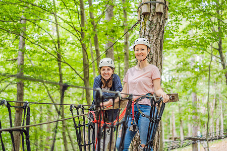 两名女性女孩在森林中的极端公路手推车滑索中滑行，在树上的登山扣安全连接到树顶绳索冒险公园。