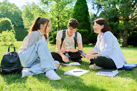 心理治疗摄影照片_学校老师、心理学家、社会工作者与青少年交谈，坐在草地上