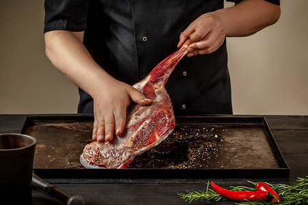 蒸羊腿摄影照片_男厨师在木桌上的石盘上用盐和胡椒摩擦生羊腿。
