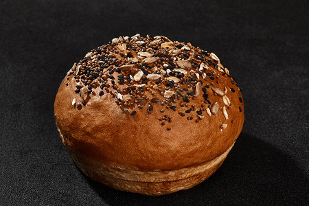撒芝麻摄影照片_新鲜可口的烤面包撒上芝麻和葵花籽，背景为黑色，有复制空间。