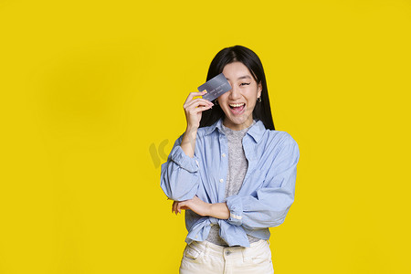 花钱买快乐摄影照片_兴奋的亚洲女孩微笑着用银行卡右眼遮住她准备花钱。