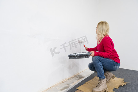 女人在搬进公寓时用滚筒设备粉刷墙壁。