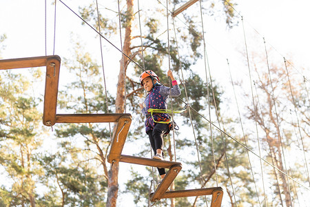 障碍训练场摄影照片_冒险乐园中的女孩攀爬是一个可以包含多种元素的地方，例如绳索攀爬练习、障碍训练场和高空滑索。