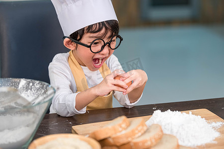 兴奋的鸡蛋摄影照片_肖像可爱的亚洲小快乐男孩对如何在家庭厨房里有趣地打破或破解鸡蛋感到惊讶和感兴趣。
