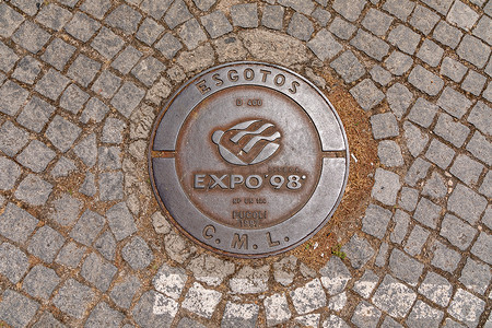 井盖摄影照片_葡萄牙里斯本世博会场地鹅卵石街道上标有 Expo 98 的井盖