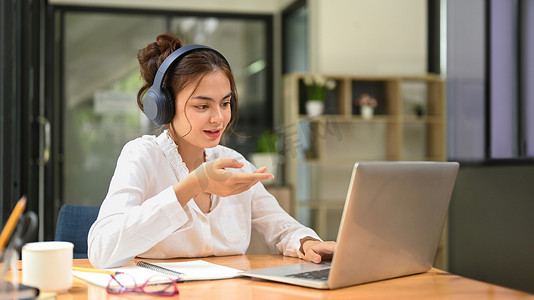 年轻女员工戴着耳机，通过笔记本电脑上的视频会议进行交流