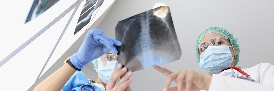 身穿医疗服的医生在诊所检查患者肺部的 X 光片