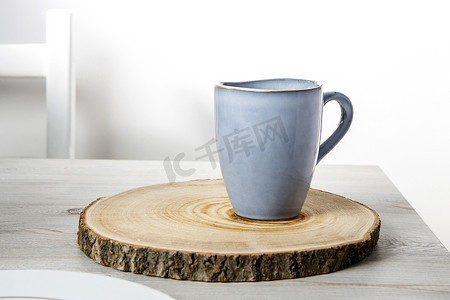 一个蓝色的陶瓷杯放在一个木制的圆形切割上，在米色的桌子上靠着白色的墙壁。