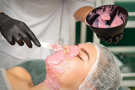 美容师在美容院一位年轻女士的脸上敷上藻酸盐面膜。