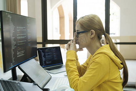 年轻女子用双手捂住脸，承受着工作编码和编程软件的压力。