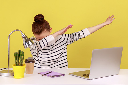 双人舞舞蹈摄影照片_极其兴奋的女上班族拿着笔记本电脑坐在工作场所，表现出轻快的舞蹈姿势。